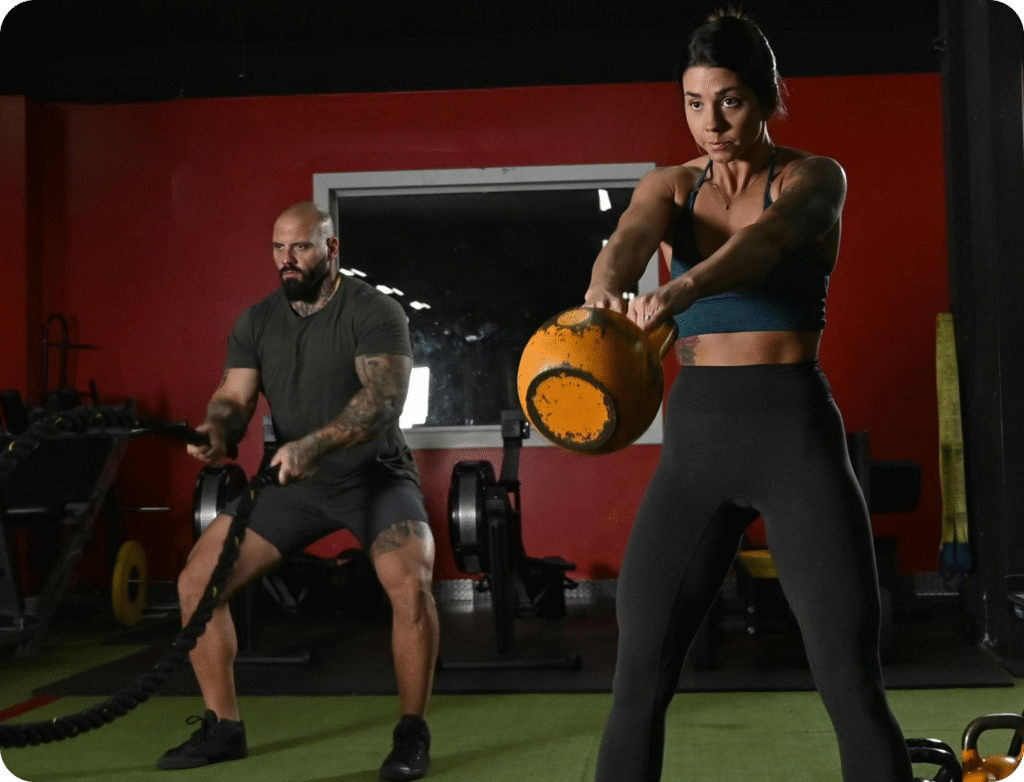 Man using battle ropes and woman swinging a kettlebell in a strength training gym session at Higher Standards.