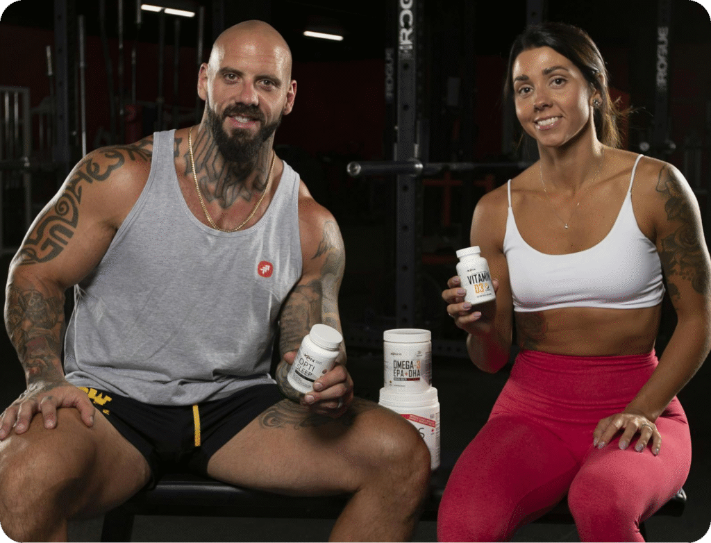 Fit man and woman seated in a gym, smiling and holding supplement bottles including Vitamin D3 and Omega 3.