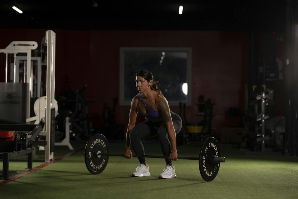 Focused woman preparing to lift a barbell in a gym setting, highlighting strength and proper form.