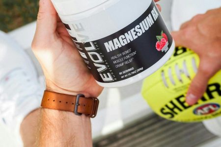 Person holding a container of Evolve Magnesium RX supplement next to a football and white sneakers.