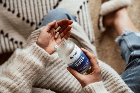 Woman in cozy clothing holding a bottle of UNPLUG nighttime recovery supplement while relaxing at home.